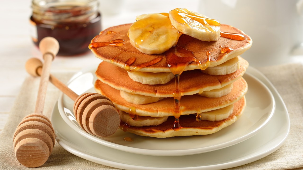 Uma pilha de panquecas servida com banana e mel.