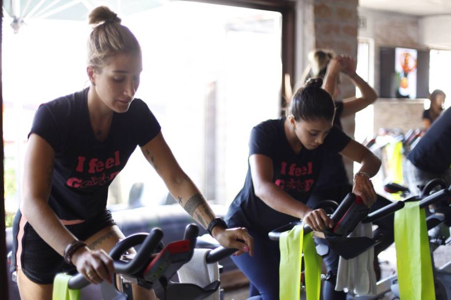 Gabi Pugliesi e Bruna Vilela pedalam na bike durante aula do Studio Velocity