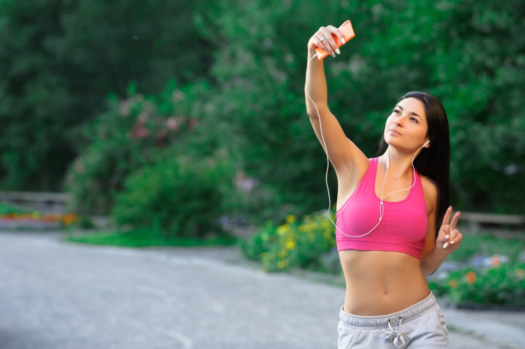 Mulher com roupa fitness tirando selfie com o celular na mão