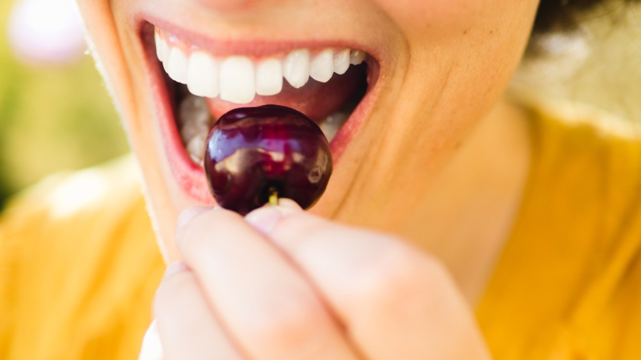 Mulher segurando uma cereja com dentes brancos