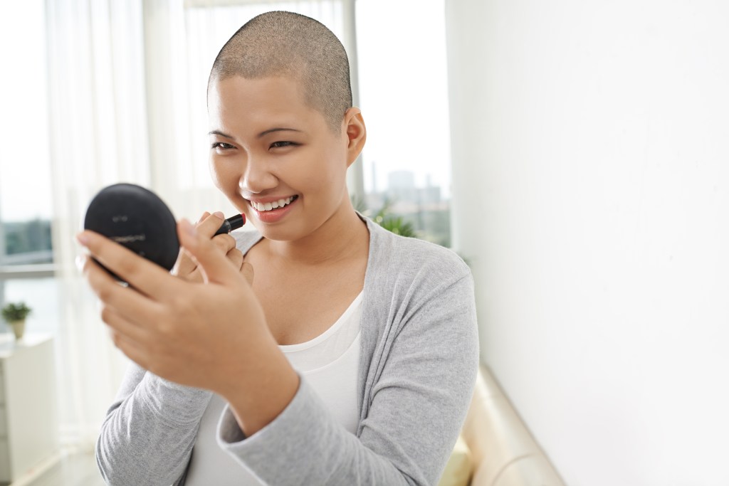 Mulher careca com cancer de mama passando maquiagem