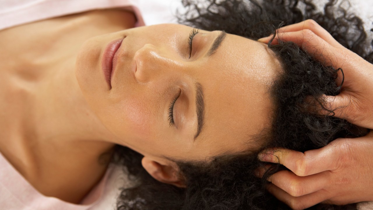 Mulher deitada na maca recebendo massagem no couro cabeludo