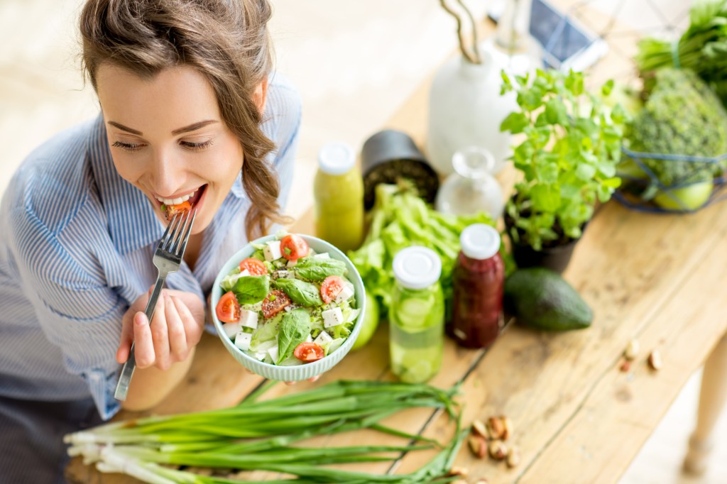 Mulher comendo um bowl com salada, tomate e queijo vegano