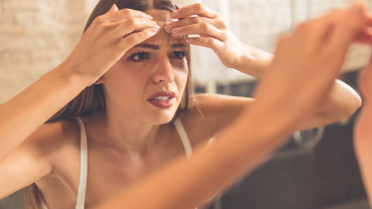 Mulher estressada olhando a pele do rosto no espelho