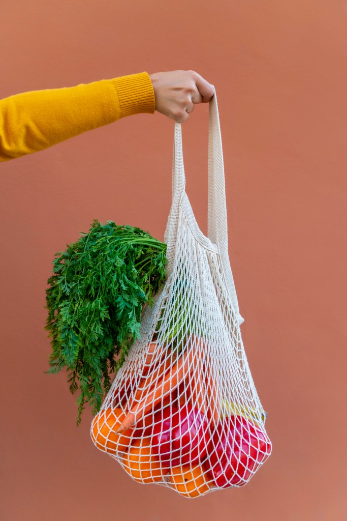 Woman Holding Reusable Cotton Mesh Bag With Fruit And Vegetables -