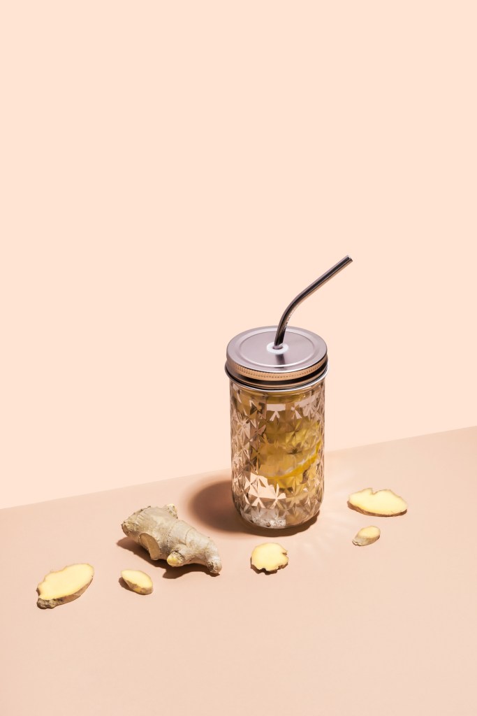 Immune Strengthening Drink. Ginger water in stylish jar with metal straw on geometric paper background and ginger slices, isometric view -