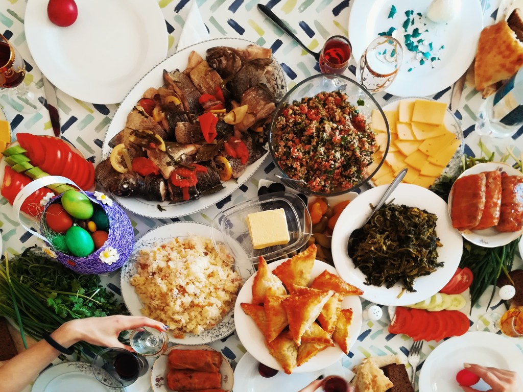 Mesa com diversos pratos de natal, no canto uma mão segura uma taça de bebida