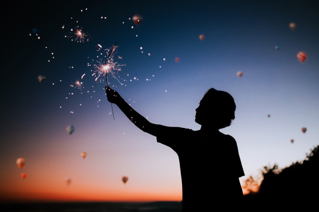 pexels-matheus-bertelli-573241 Silhueta de uma pessoa com o céu de fim da tarde ao fundo. A pessoa segura uma vela com a mão para cima