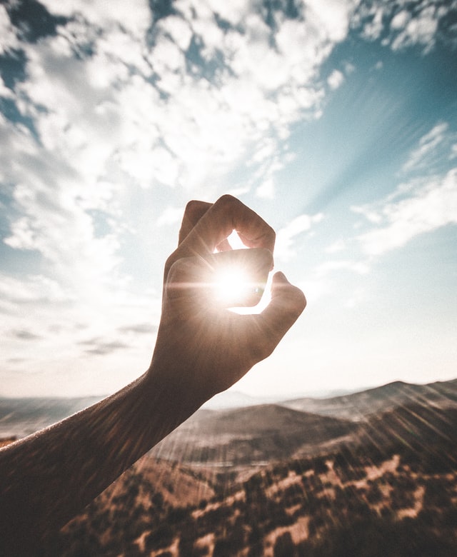 uma mão fazendo o contorno do sol em uma área montanhosa