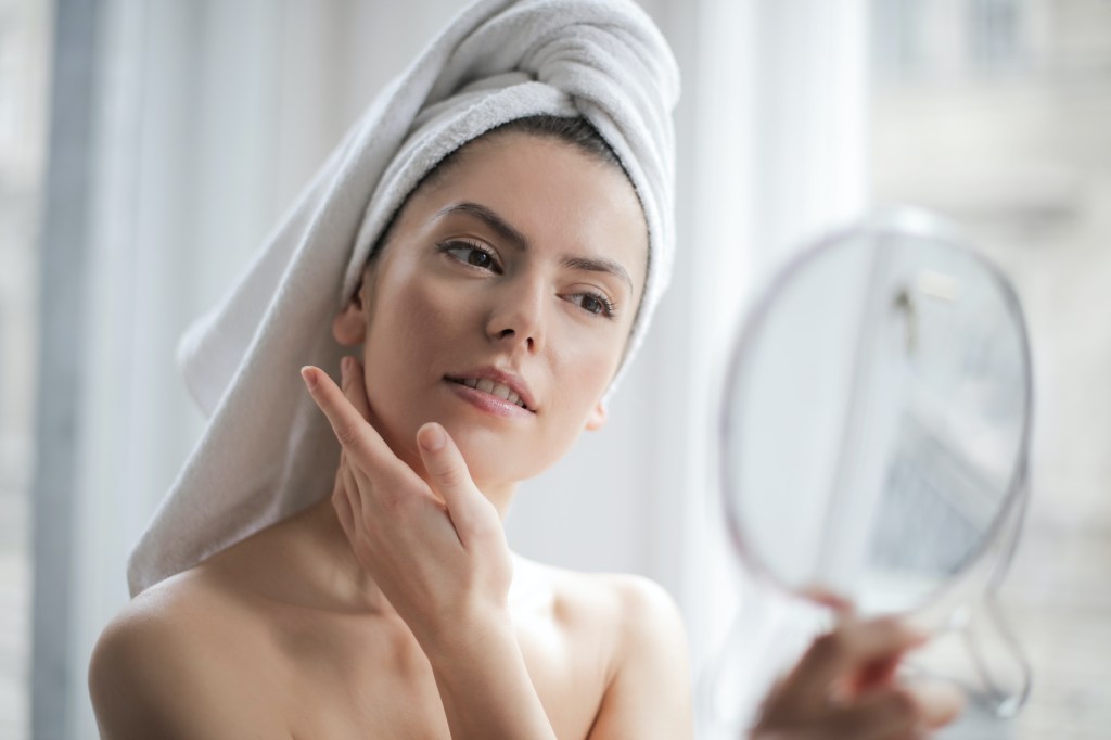 Foto ilustrativa mostra uma mulher analisando a sua pele em frente a um espelho. Matéria fala como o açúcar afeta a pele.