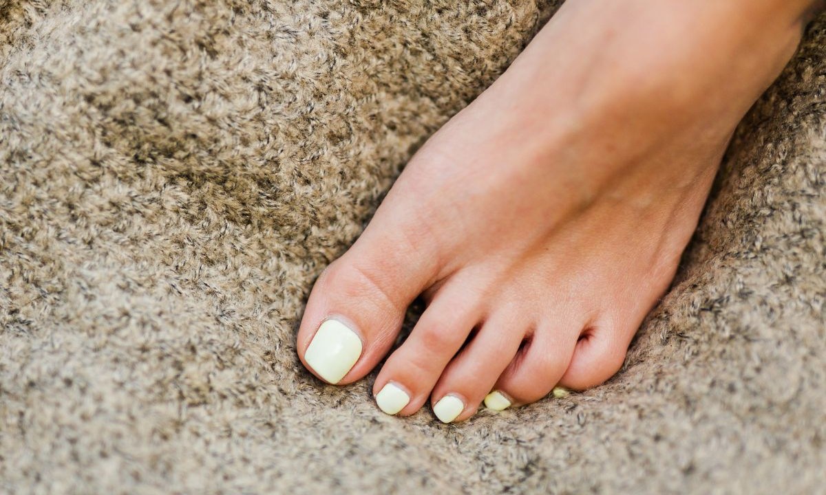 Pé com as unhas pintadas apoiado em superfície marrom