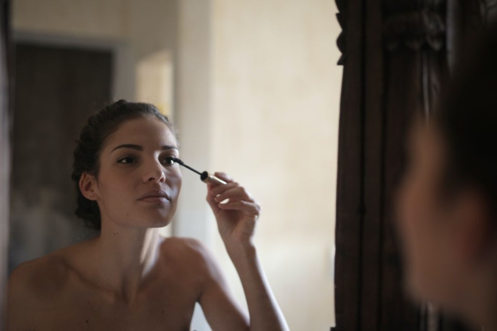 Mulher aplicando rímel em frente ao espelho