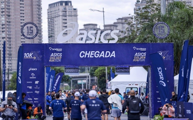 Corredores cruzam a linha de chegada da Asics Golden Run 2026, um portal azul com o logo Asics e a palavra 